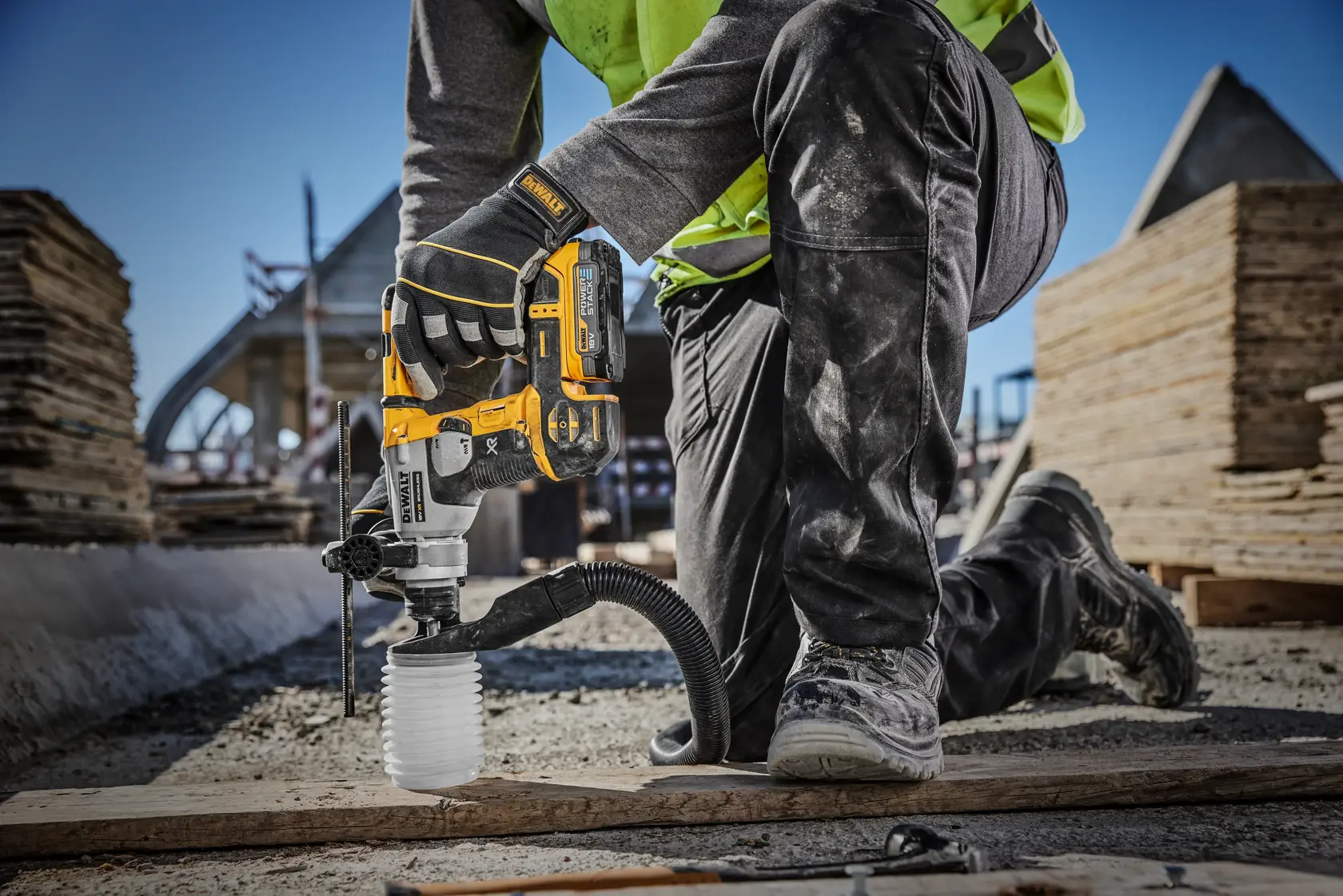 Una persona con casco de seguridad y chaleco de alta visibilidad está utilizando un taladro rotativo inalámbrico DEWALT para perforar una pared, con equipo de extracción de polvo acoplado. El taladro tiene las marcas XR y Power Stack.