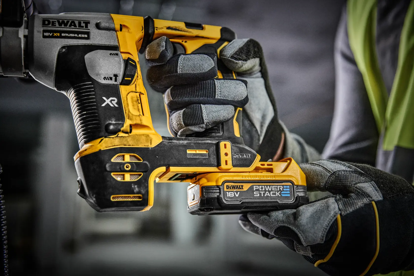 Un trabajador de la construcción está usando un martillo perforador inalámbrico DEWALT (modelo DCH172E2T) con extracción de polvo en una obra, perforando el suelo mientras se arrodilla.