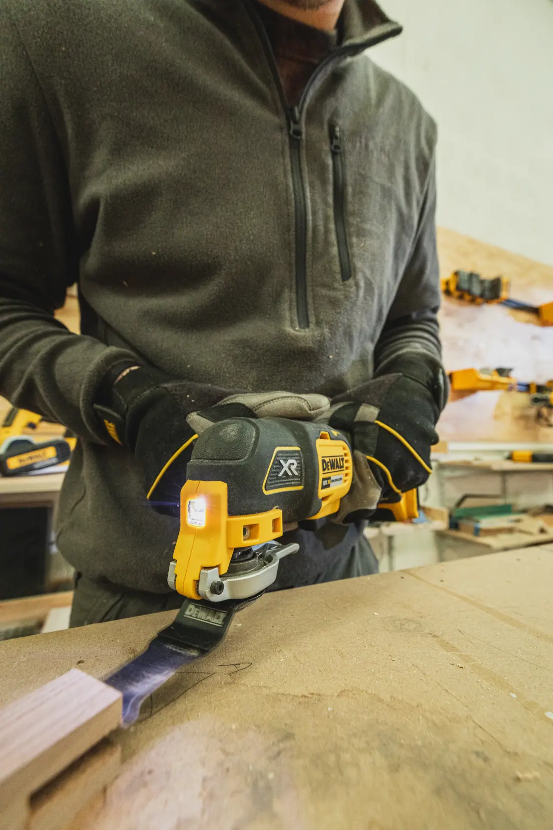 Person uses DEWALT DCS355N-XJ oscillating tool on wood in a workshop.