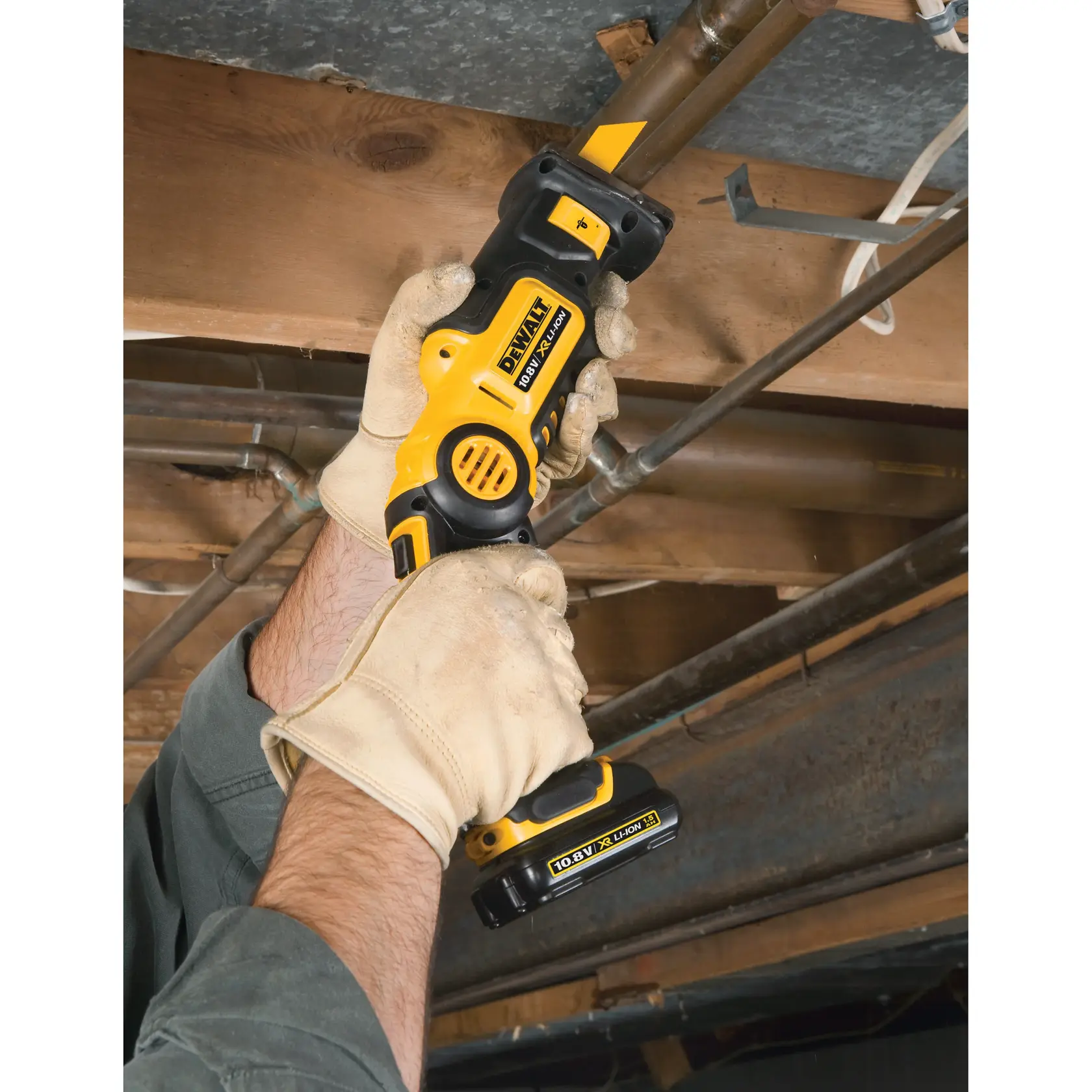 Manos enguantadas usan una sierra recíproca DEWALT inalámbrica para cortar un tubo bajo vigas de madera.