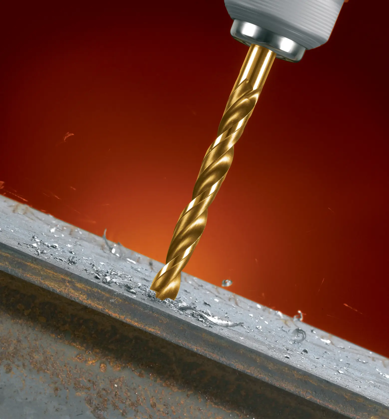 Primer plano de una broca dorada de metal conectada a un taladro, perforando una superficie metálica con virutas de metal dispersas alrededor.