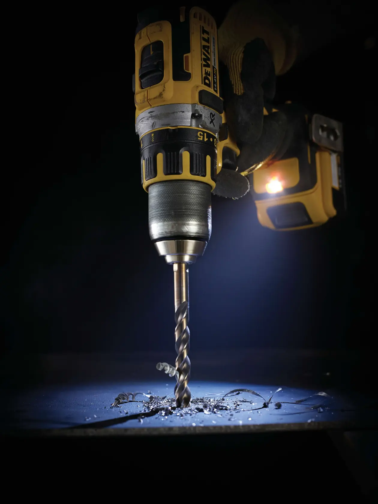 Taladro inalámbrico DEWALT perforando metal, luz y virutas visibles sobre fondo oscuro.