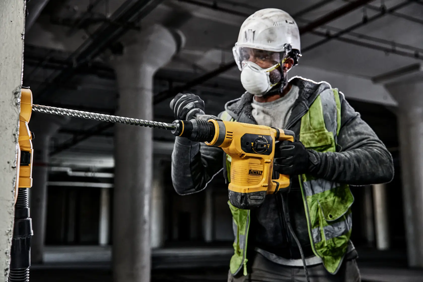Ein Bauarbeiter mit Schutzausrüstung benutzt einen gelben DEWALT-Bohrhammer, um eine Betonsäule auf einer Baustelle zu bohren.