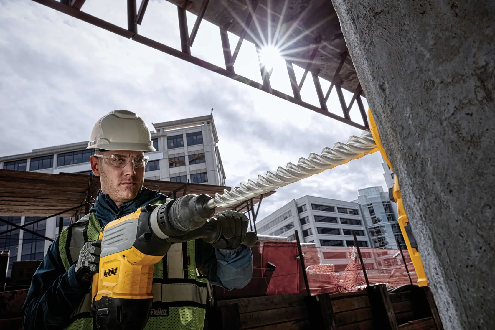 Arbeiter nutzt DEWALT DT60815 Bohrer auf Baustelle, Gebäude im Hintergrund sichtbar.