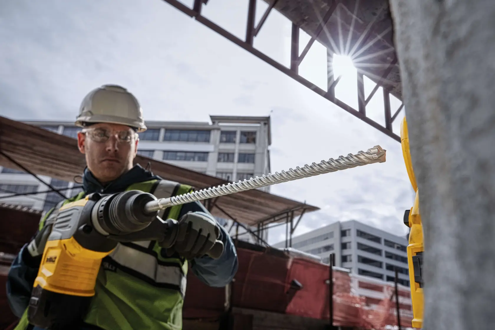 Person nutzt einen DEWALT Schlagbohrer mit Staubabsaugung auf Betonboden an einer Baustelle.