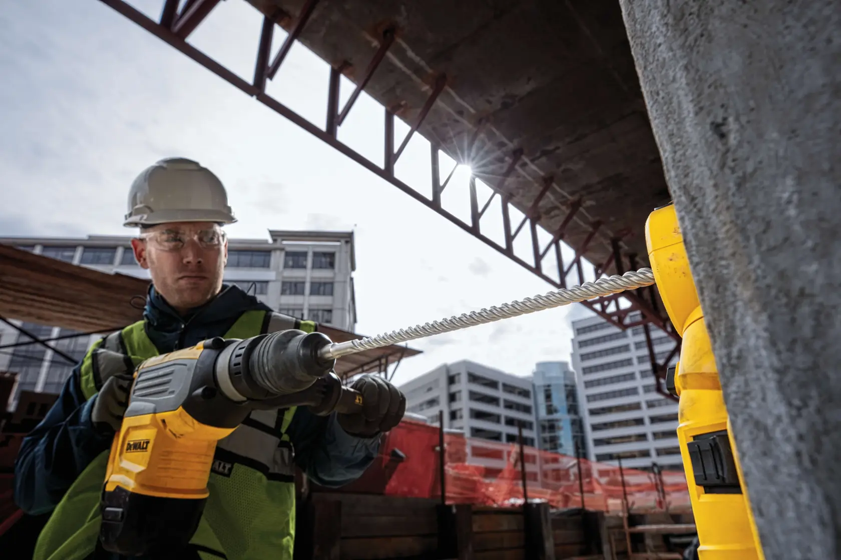 Trabajador usa taladro DEWALT en construcción con edificios detrás.