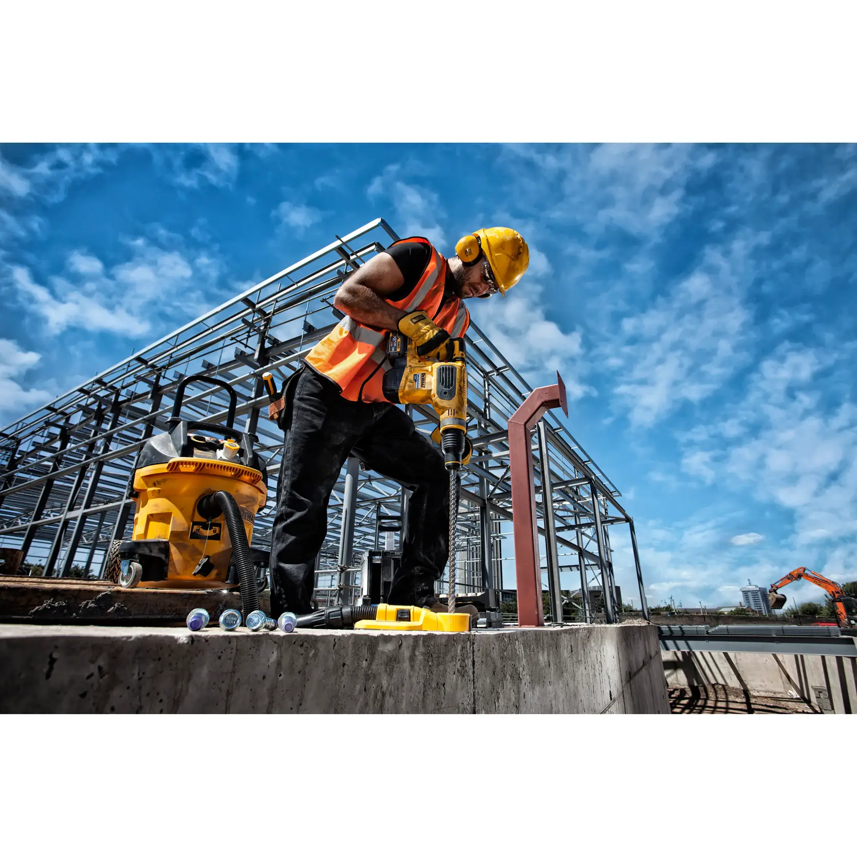 Trabajador usa taladro DEWALT en obra con estructuras de acero y equipos bajo cielo azul.