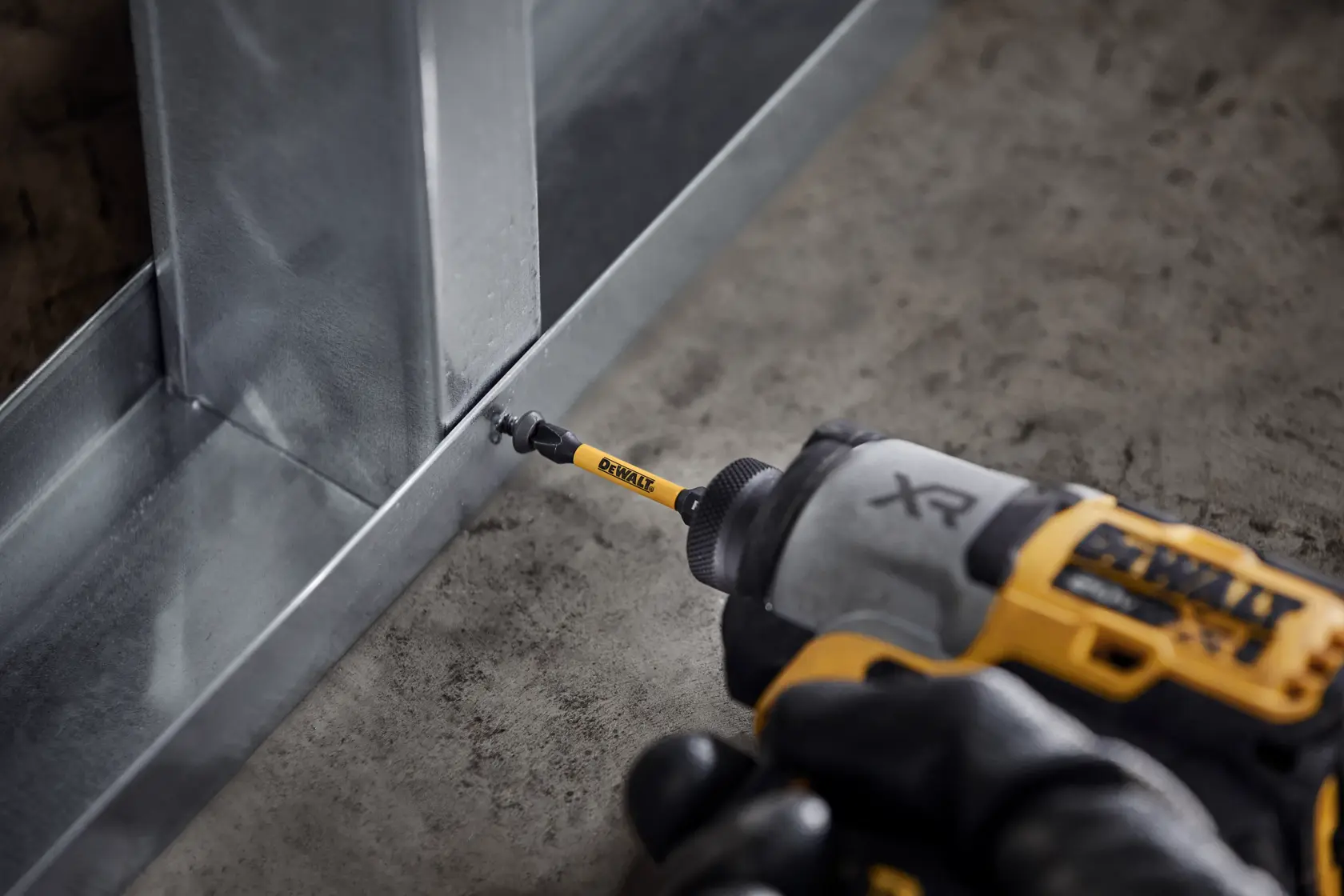 DEWALT-Bohrer schraubt eine Schraube in einen Metallrahmen, Nahaufnahme auf Betonboden.