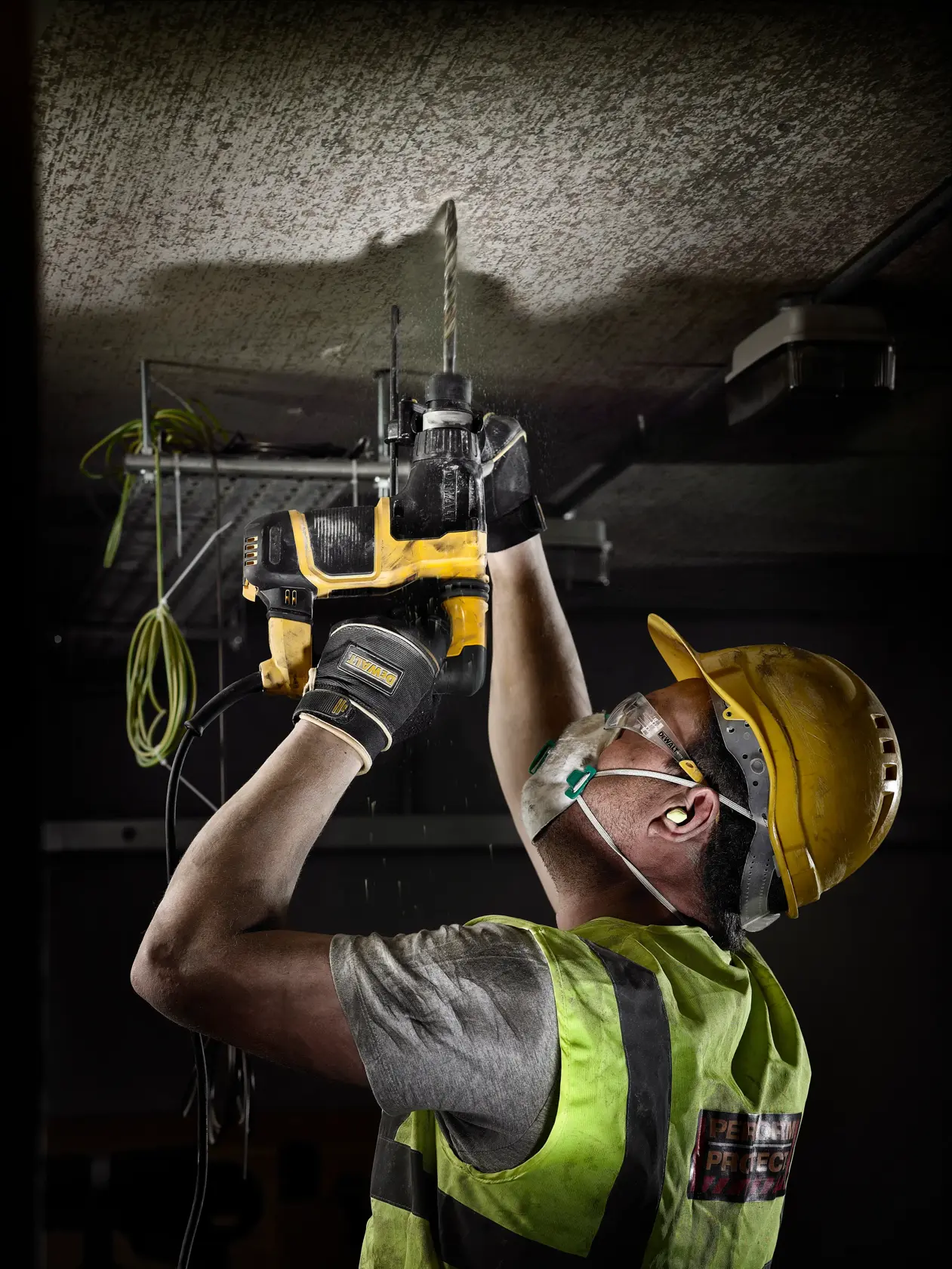 Trabajador con equipo de seguridad usa taladro DEWALT para perforar el techo en obra.
