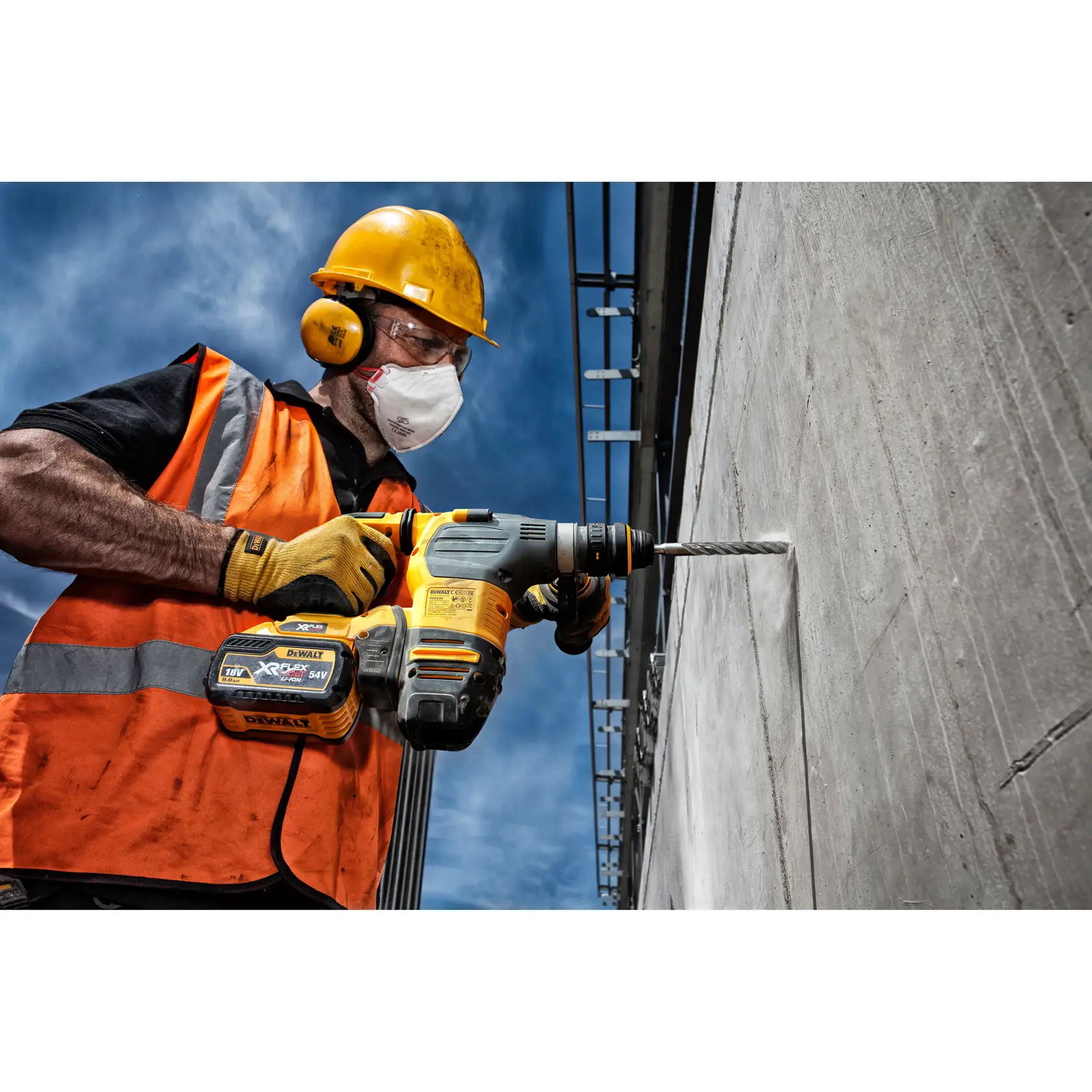 Trabajador con protección usa taladro inalámbrico DEWALT para perforar pared de concreto al aire libre.