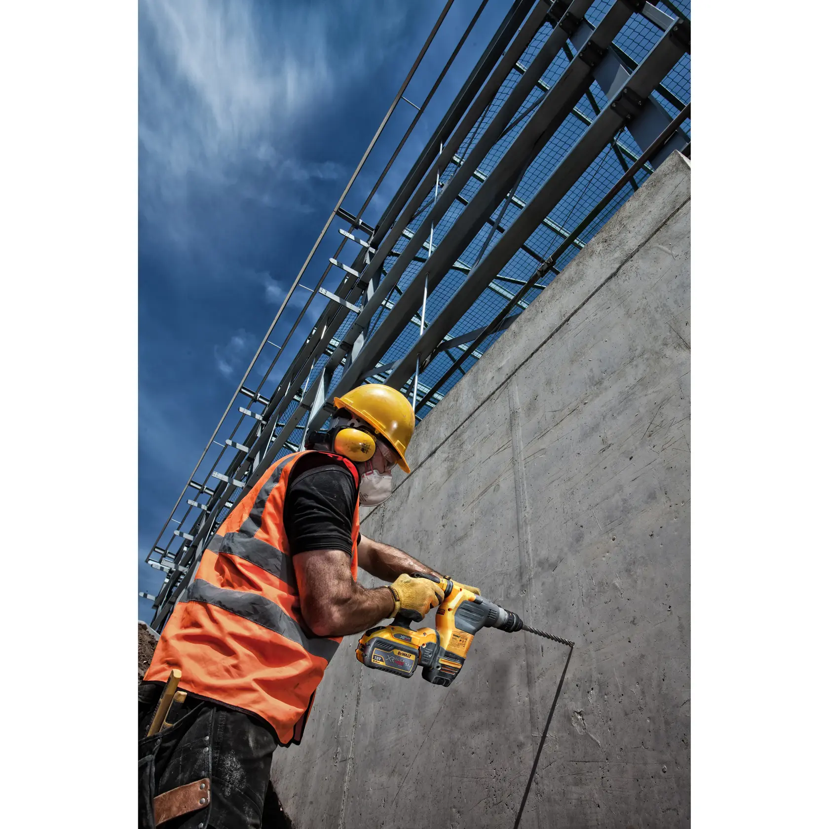 Trabajador perfora muro de cemento con taladro DEWALT, lleva chaleco naranja y casco amarillo.